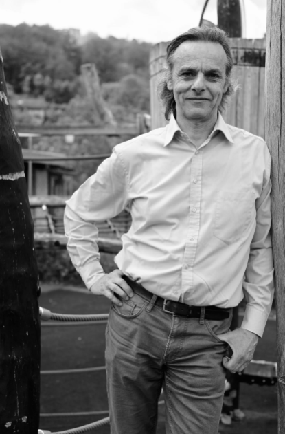 Ein Mann (Dieter Fauth) lehnt an einer Holzwand und schaut in die Kamera